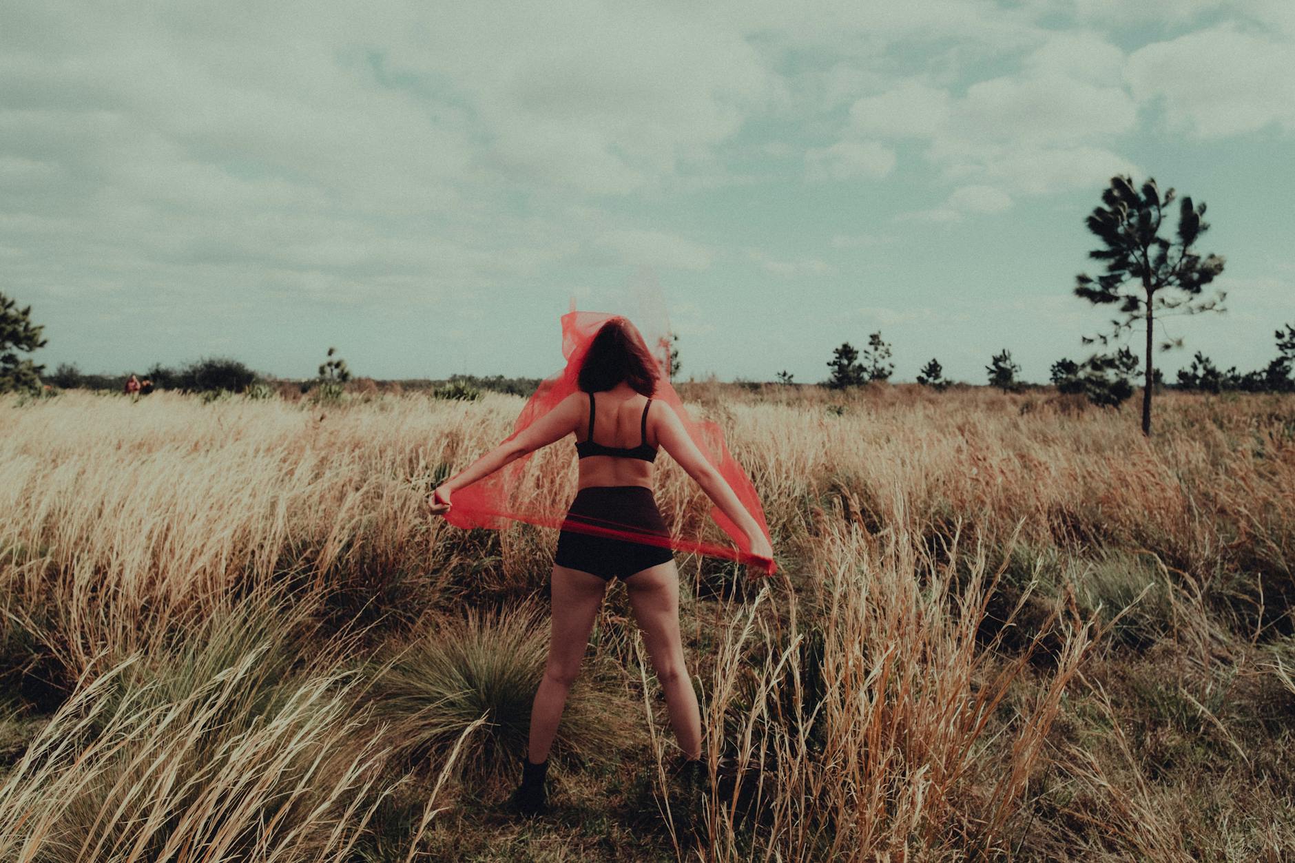 woman wearing bra and holding red scarf on a field