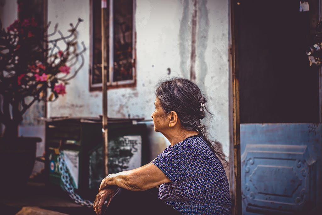 Elderly woman sitting by a doorway, gazing thoughtfully outdoors yearning for the days before she was too old to travel solo