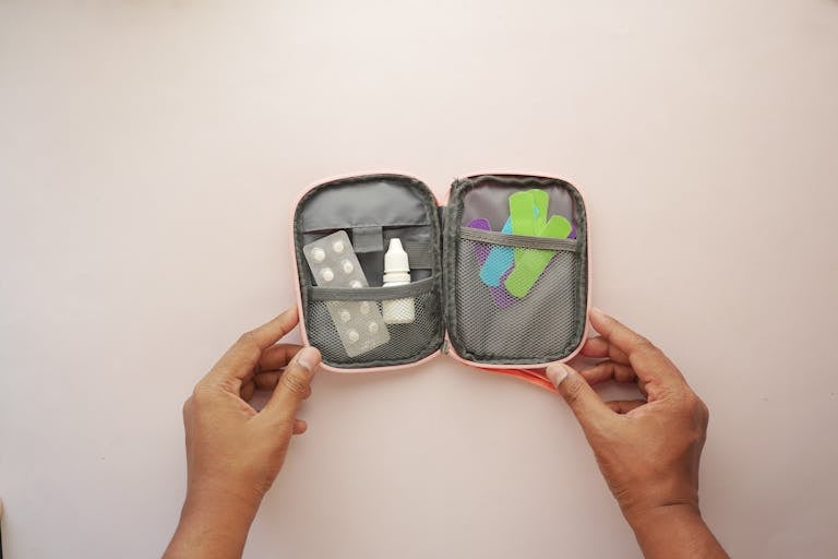 Open travel medical kit containing band aids, tablets, and medicines, held by hands.