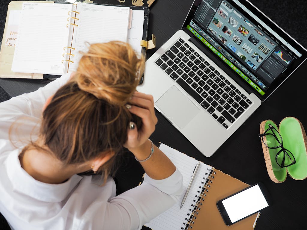 Overhead view of a sick woman working at a desk with a laptop, phone, and staying in touch with her family when getting sick while travelling solo