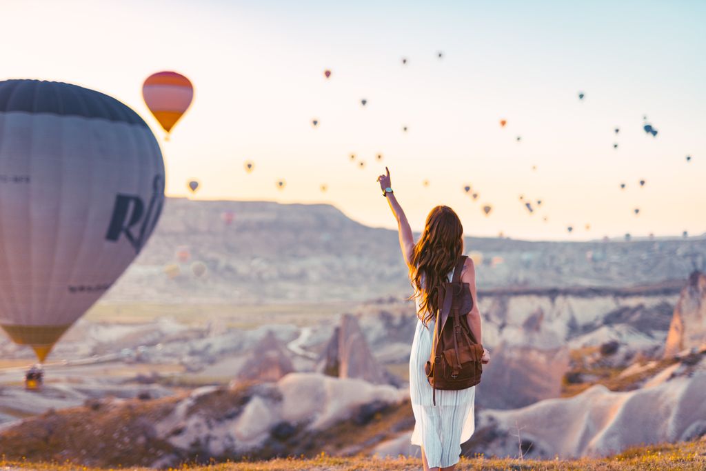A woman points at colorful hot air balloons over Cappadocia at sunrise.  Put this on your travel bucket list